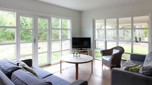 A spacious living room with a large TV, two sofas, a round table, and large windows offering a view of greenery. - "Borica" - 100m from the sea by Interhome (Væggerløse)