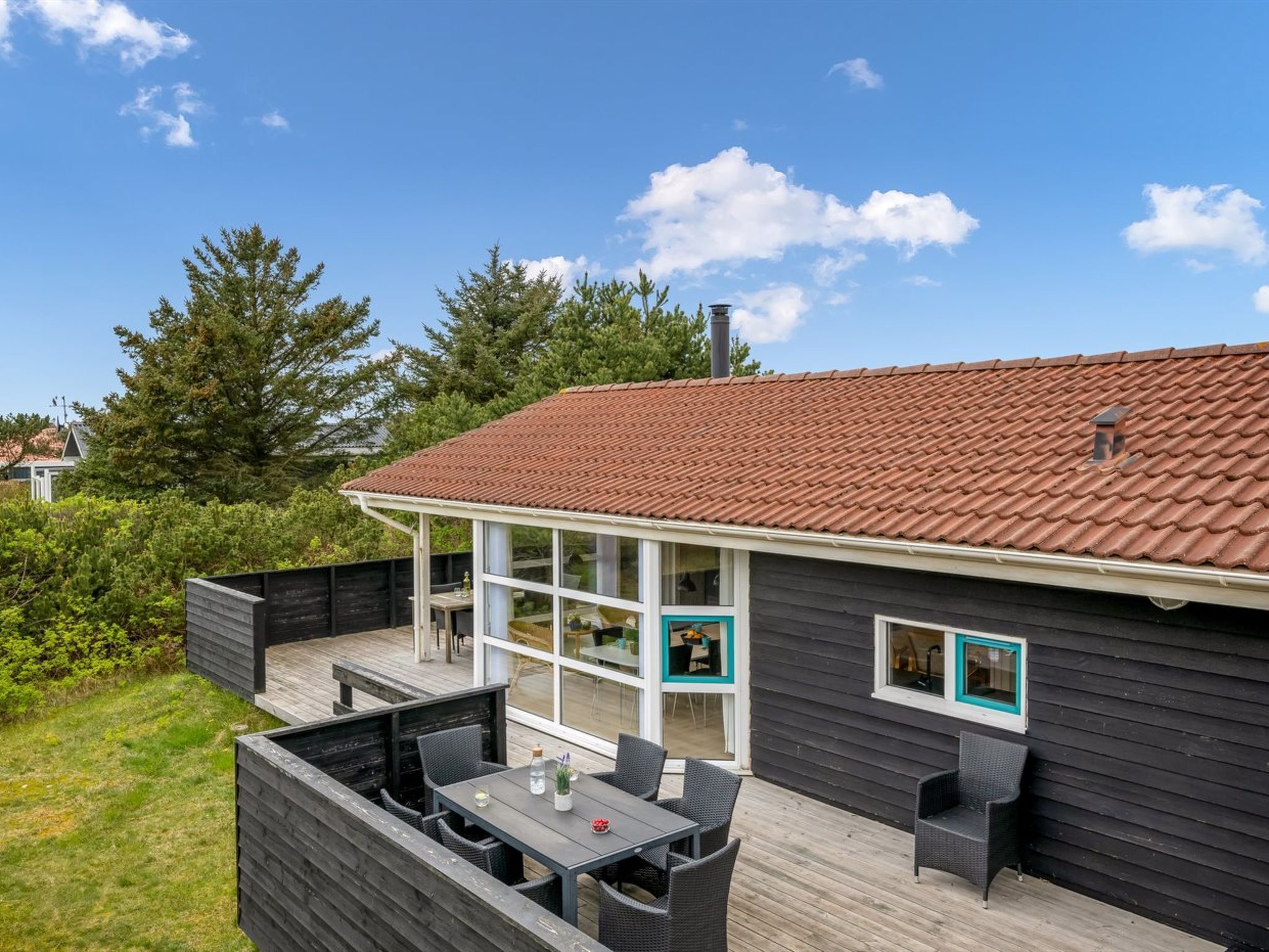 A modern house with a deck, a dining area, and a large window overlooking a garden.