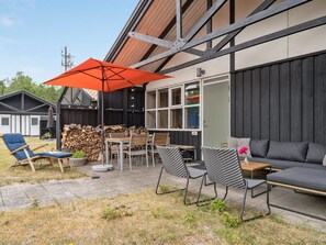 Un patio al aire libre con una mesa de comedor, sillas, un sofá y un paraguas naranja.