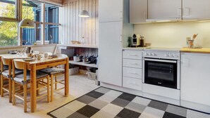 A modern kitchen with white cabinets, a wooden dining table with chairs, and a large window with blue shutters. - "Robert" - 250m from the sea by Interhome (Væggerløse)
