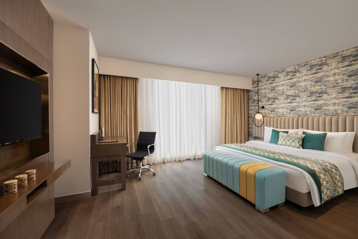 Een hotelkamer met een groot bed, een bureau, een stoel, een televisie en een groot raam met gordijnen.