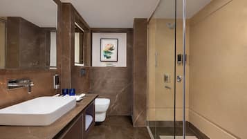 A modern bathroom with a large white sink, a glass shower enclosure, and a marble-tiled floor.