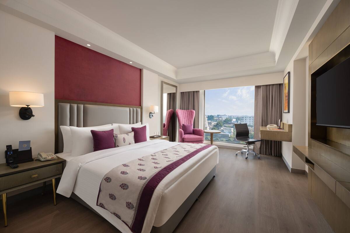 Een moderne hotelkamer met een groot bed, een bureau, een stoel, een televisie en uitzicht over de stad.