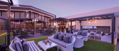 A modern outdoor seating area with a bar and dining space, featuring wicker furniture and a well-maintained lawn.