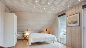 A bedroom with a wooden ceiling, a bed, a nightstand with a lamp, a window, and a door. - "Gertrudis" - 2km to the fjord by Interhome (Frøstrup)