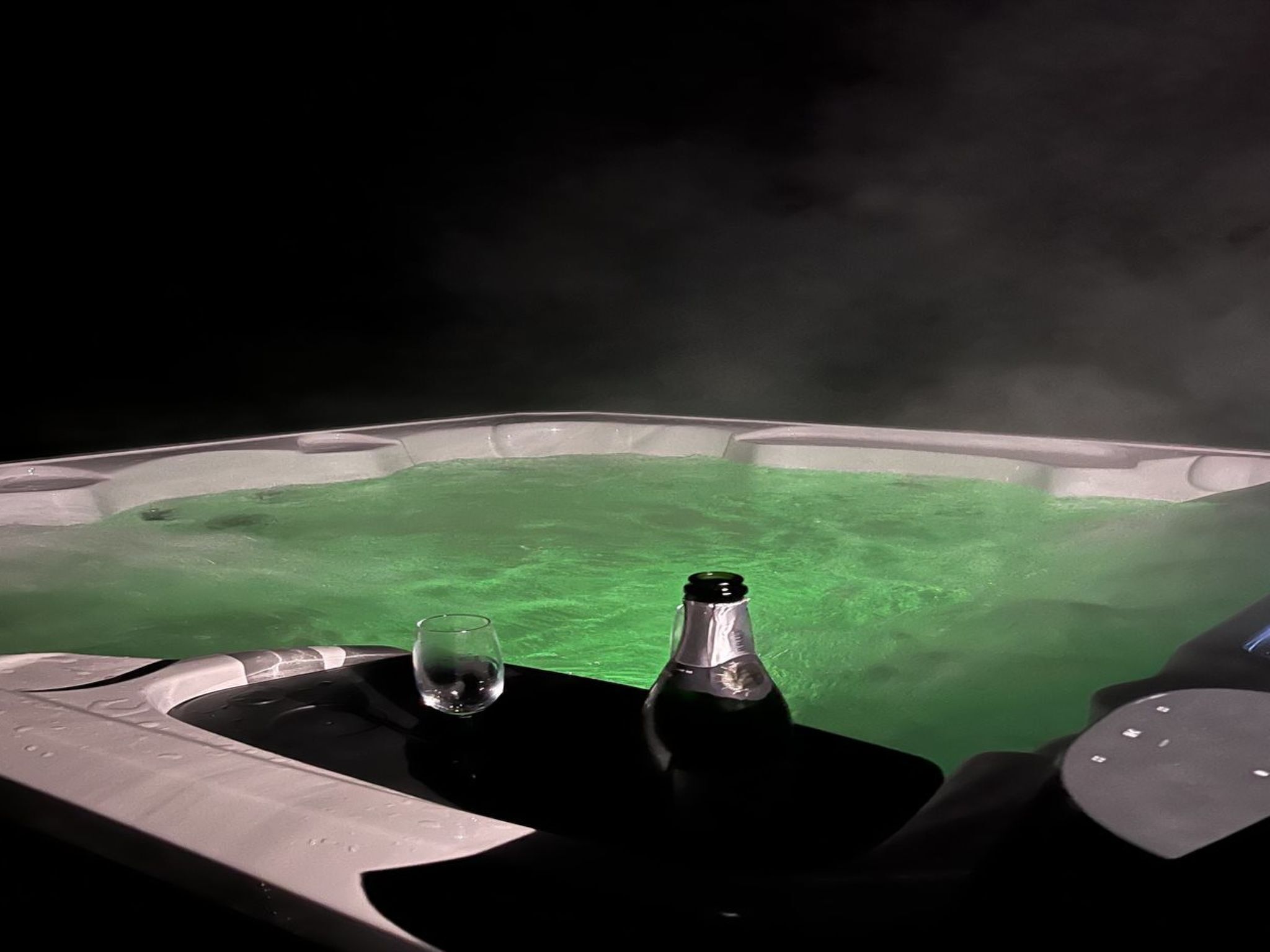 A hot tub with a glass and bottle on a tray.