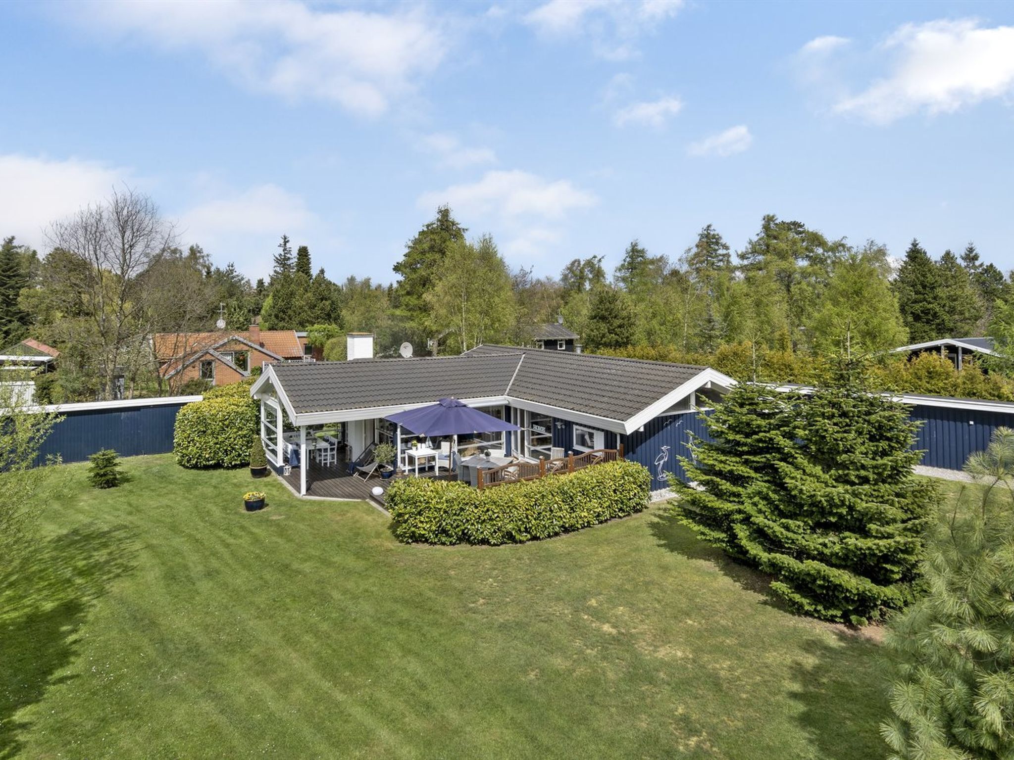 A two-story house with a covered patio, a fenced yard, and a large tree in the foreground.