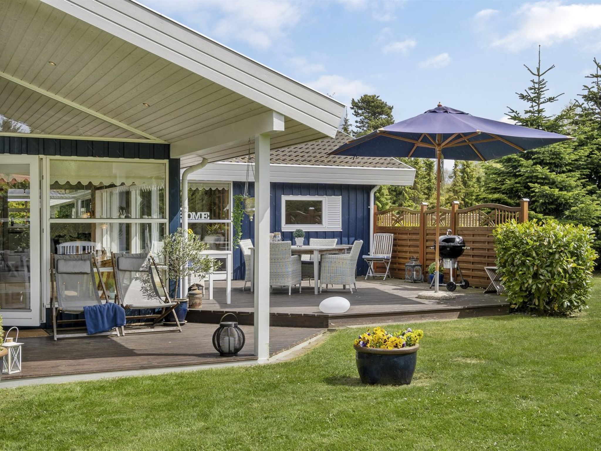 Un patio couvert avec des sièges d’extérieur, un barbecue et un grand parasol.