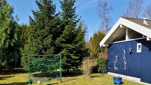En blå byggnad med ett vitt tak, ett fotbollsmål och ett träd i bakgrunden.