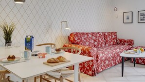 Una sala de estar moderna con una mesa blanca, un sofá rojo estampado con flores e iluminación colgante.