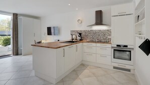 Una cocina moderna con armarios blancos, encimera de madera, salpicadero azulejado y horno empotrado.