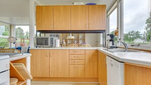 A modern kitchen with wooden cabinets, a microwave, a coffee machine, and a large window providing a view of the outdoors.