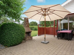 Une terrasse extérieure avec une cheminée en pierre, une table avec des chaises et un grand parasol.
