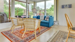 A spacious living room with large windows, a blue sofa, wicker chairs, and a patterned rug.