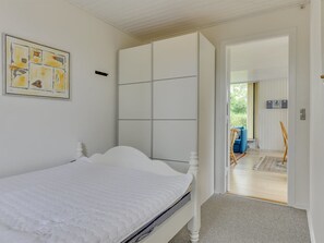 Une chambre à coucher comprenant un lit, une armoire et une porte donnant sur un balcon où se trouvent une chaise bleue et une chaise en osier.