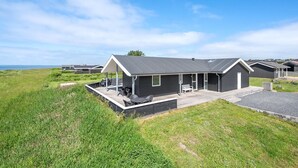 Une caravane moderne dotée d’un patio couvert, entourée de prairies verdoyantes et surplombant un ciel dégagé.