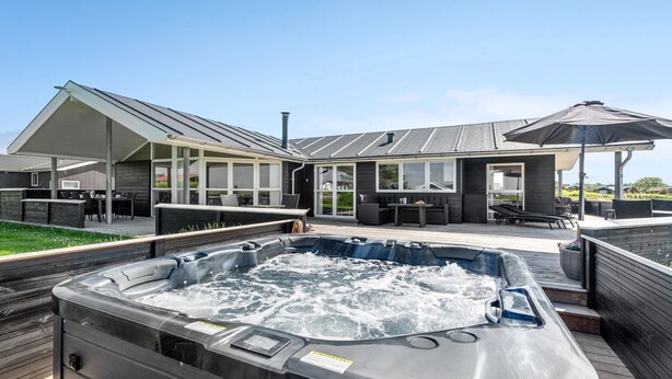 Un espace moderne aménagé à l’extérieur avec un bain à remous, une terrasse en bois, un coin salon couvert et un grand parasol.
