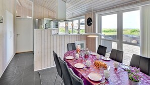 Un coin repas avec une table dressée pour quatre personnes, une cuisine en arrière-plan et une vue sur l’extérieur.
