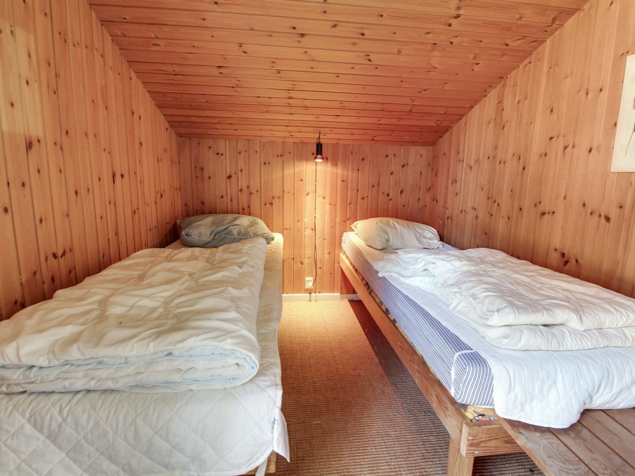 A small, wooden-paneled room with two single beds, each with a pillow and a blanket.