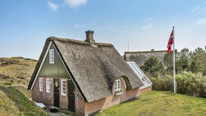 A traditional thatched-roof house with a small porch, a flagpole with a flag, and a grassy landscape. - "Dordi" - 300m from the sea by Interhome (Fanø)