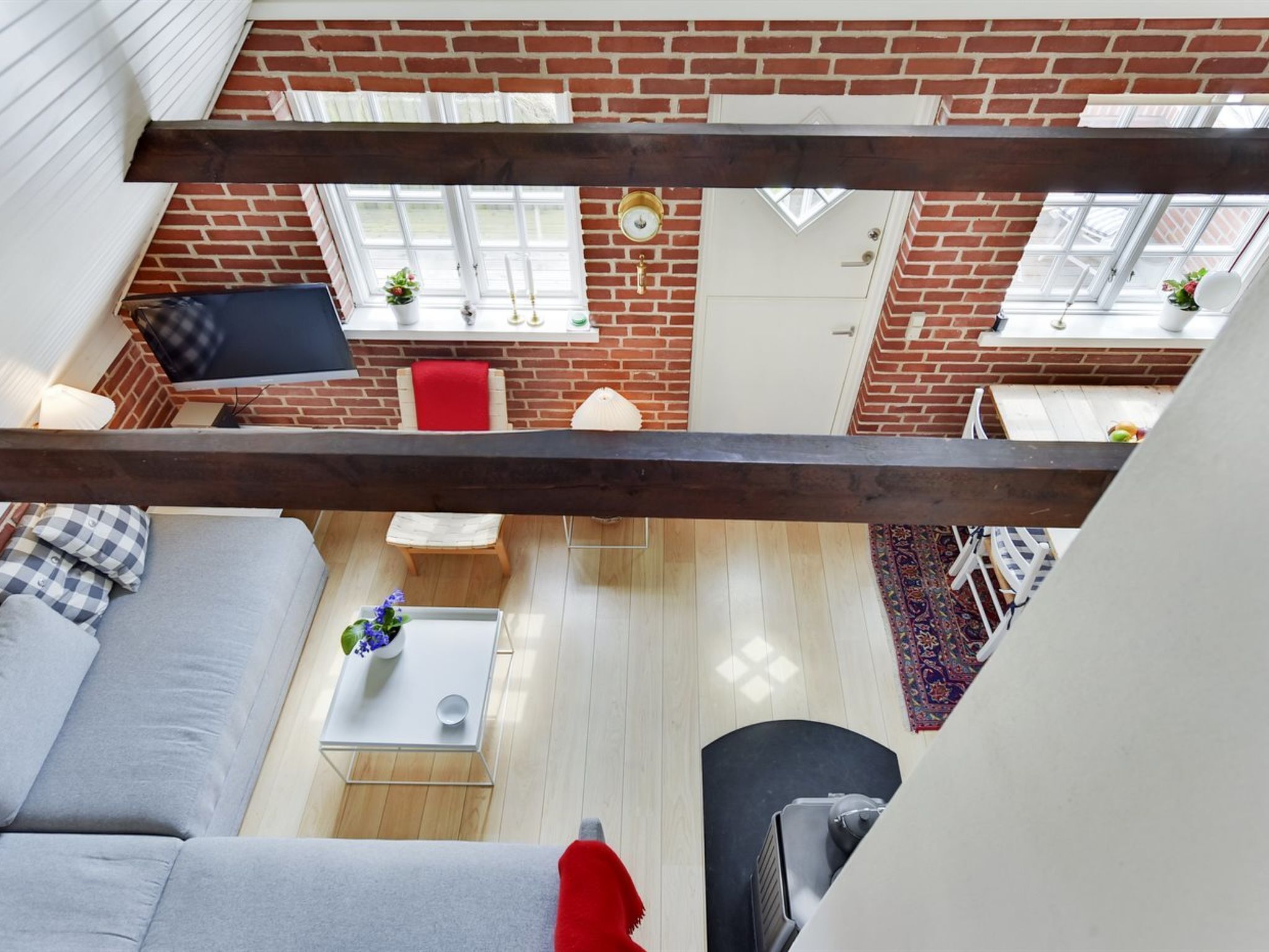 Una habitación con techos altos, paredes de ladrillo visto y techo de vigas de madera, con vistas a un comedor que incluye una silla roja y una mesa blanca.