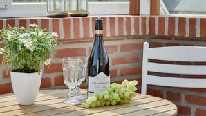 A table with a bottle of wine, glasses, a potted plant, and grapes on a balcony with brick walls and a view of greenery. - "Dordi" - 300m from the sea by Interhome (Fanø)