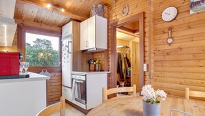 Een gezellig keuken in blokhutstijl met houten wanden, een eettafel met stoelen, een rode koffiezetapparaat en een klok aan de muur.