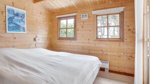 Een slaapkamer in een houten chalet, met een bed, twee ramen en een schilderij aan de muur.