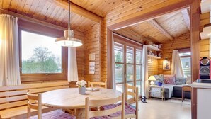 Een houten cabin met een ronde houten tafel, bankjes en een bank.