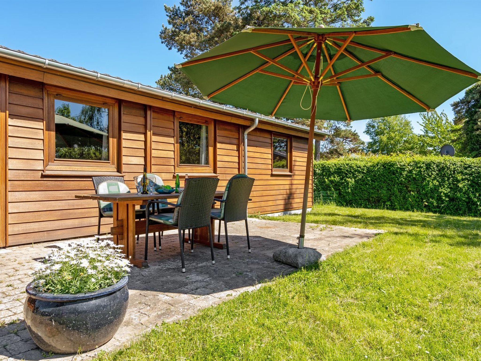 A wooden house with a patio, a table with chairs, and a large green umbrella.