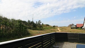 A view from a balcony with a wooden railing, overlooking a grassy area with a path leading to a house with a red roof.