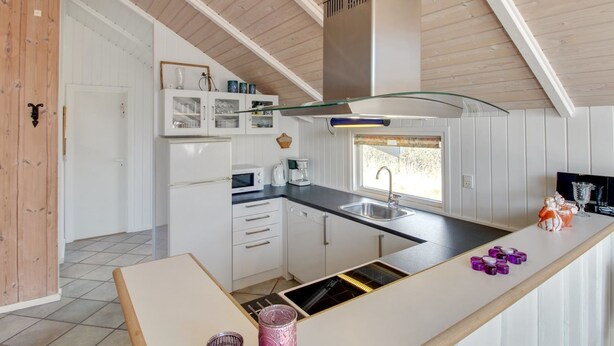 A modern kitchen with white cabinetry, a stainless steel range hood, a built-in oven, and a large island with a sink.