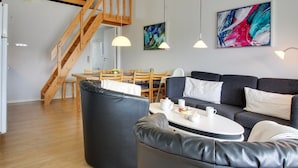 Un salon moderne avec un escalier, un coin repas et deux œuvres d’art accrochées au mur.