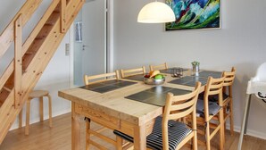 Un coin repas avec une table et des chaises en bois, un saladier rempli de fruits et un tableau accroché au mur.