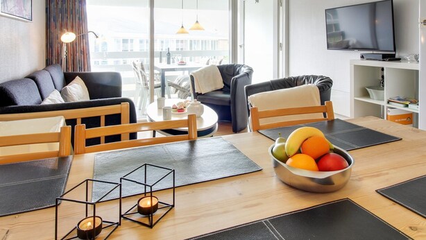 Un salon moderne avec un canapé, une table à manger avec des sets de table, un panier de fruits et un téléviseur.