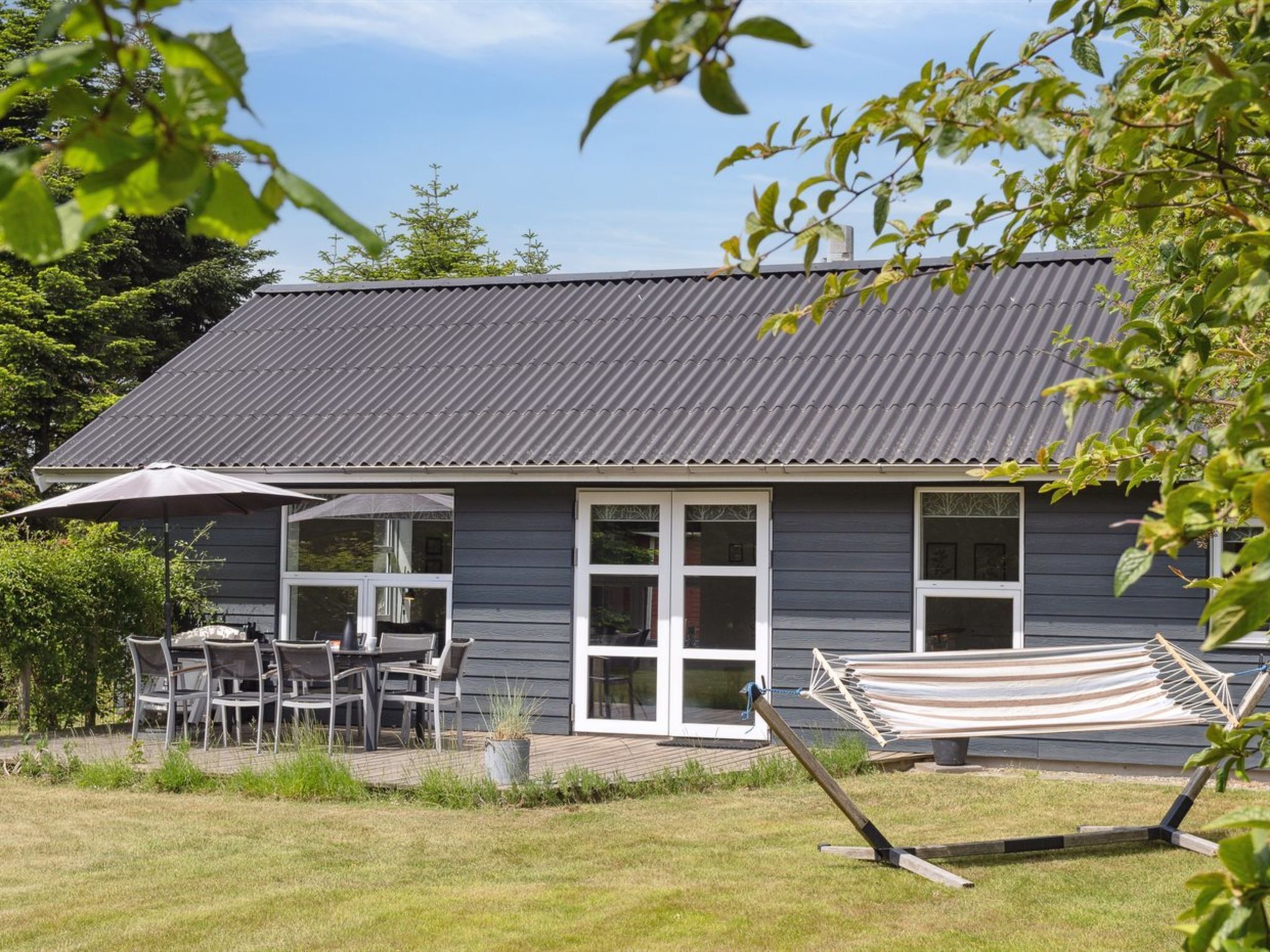 A house with a grey exterior, a tiled patio with outdoor furniture, and a hammock.