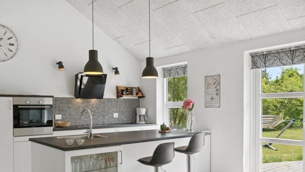 Cocina moderna con una isla central, taburetes de bar, iluminación colgante y vistas al exterior.