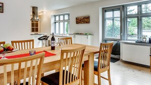 Een moderne keuken met een eethoek, met een houten tafel, stoelen en een groot raam met uitzicht op groen.