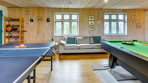 Een kamer met een tafeltennistafel, een poolbiljart, een bank en een raam met uitzicht op groen.
