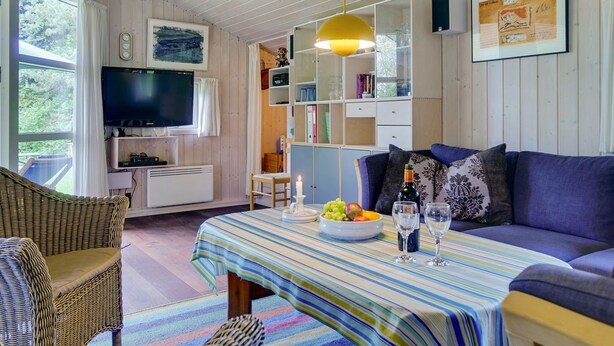 En hyggelig stue med et fjernsyn, en sofa, et spisebord med stribet dug og en reol.