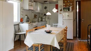 Ett kompakt kök med vita skåp, en spis och ett kylskåp. Där finns ett matbord med stolar och en liten matta på golvet.