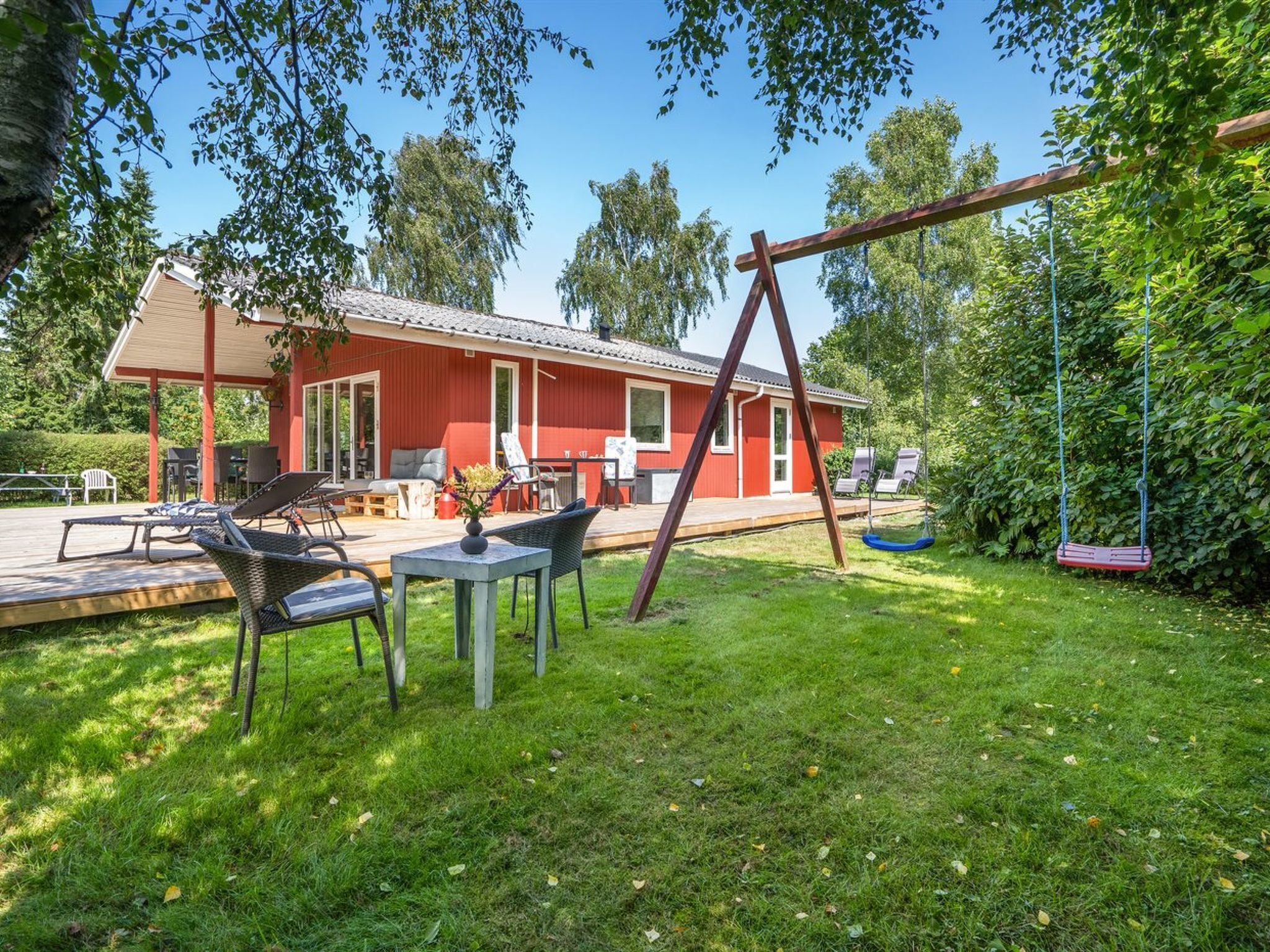 A red house with a patio, outdoor seating, and a swing set.