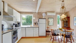 A modern kitchen with white cabinets, a built-in oven, and a dining area with a wooden table and chairs. - "Mile" - 260m from the sea by Interhome (Idestrup)