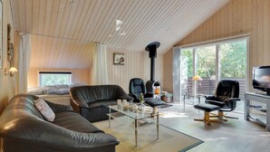 Ein gemütliches Wohnzimmer mit hohen Decken, Holzwänden, einem Kamin, Ledersofas und einem Fernseher.