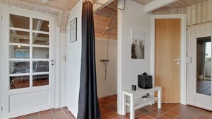 A room with a shower, a white door, and a small white table with a black bag on it.