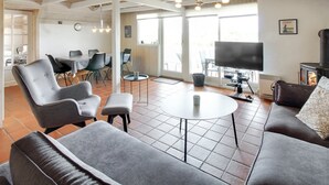 A spacious living area with a high ceiling, a fireplace, a television, and a dining area with chairs and a table.