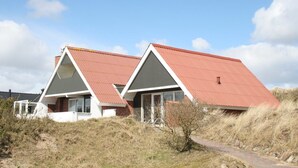 A row of two-story houses with red roofs, surrounded by dry grass and a clear sky.