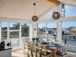 Uma zona de refeições moderna com uma mesa de madeira, cadeiras brancas e grandes janelas com vista para casas.