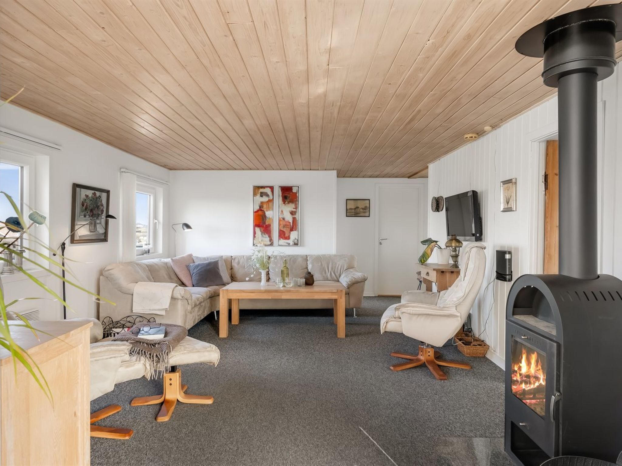 Un salon moderne avec un plafond en bois, un canapé, une table basse, une cheminée et un téléviseur fixé au mur.