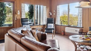 A cozy room with a leather sofa, two chairs, a round table with fruit, and large windows with curtains. - "Frode" - 400m from the sea by Interhome (Idestrup)